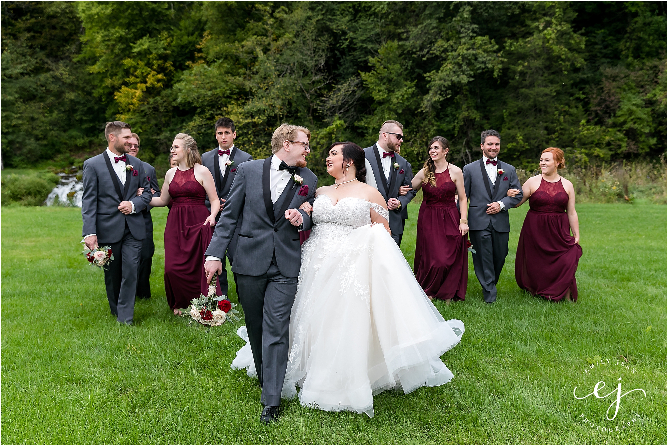 walking grey tuxedos and red dresses bridal wedding party bride and groom long veil lace grey suit dipping winnebago springs wedding venue in caledonia minnesota