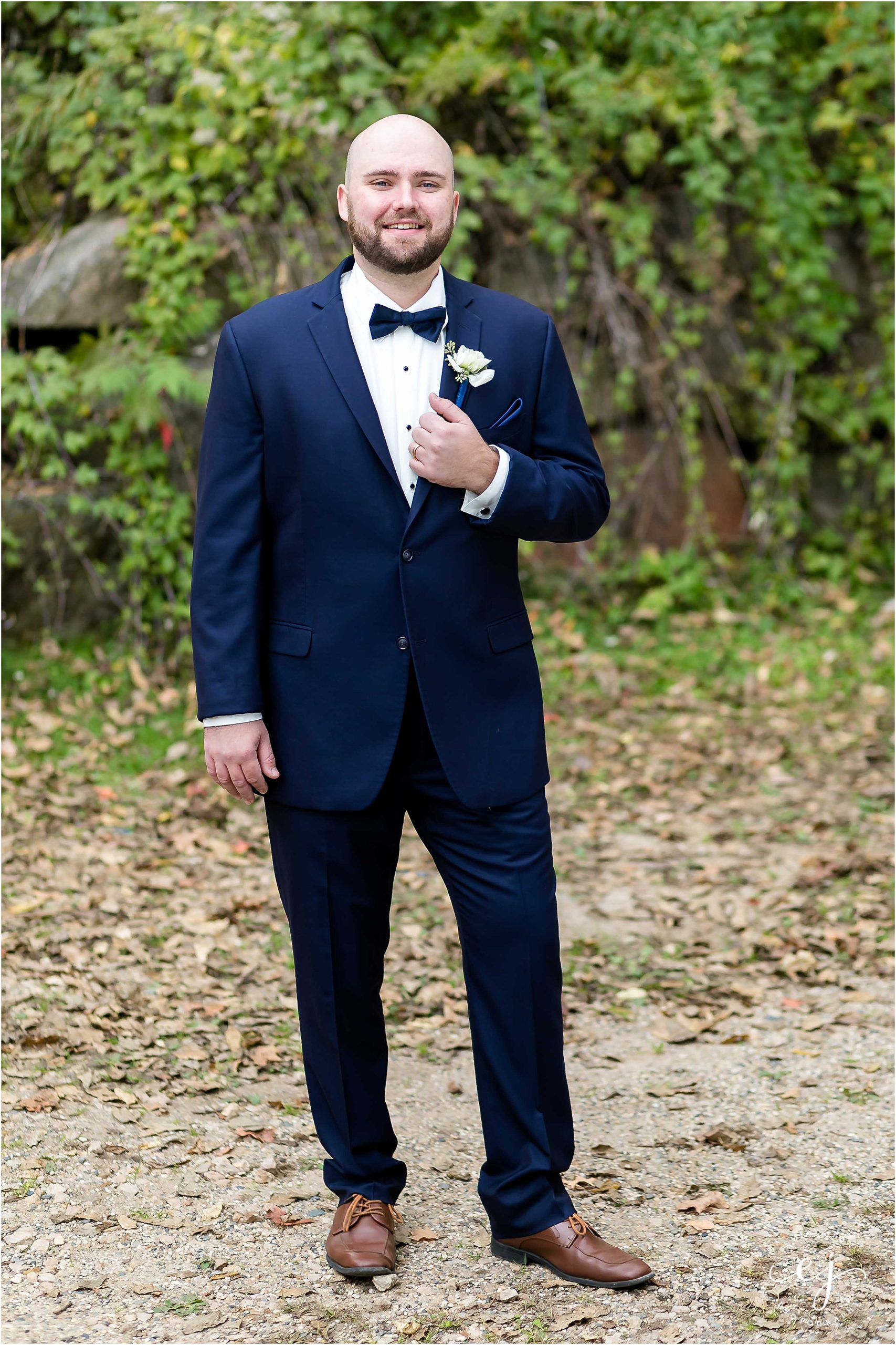Professional portrait of a groom wearing a navy tuxedo with navy bowtie and white boutonniere