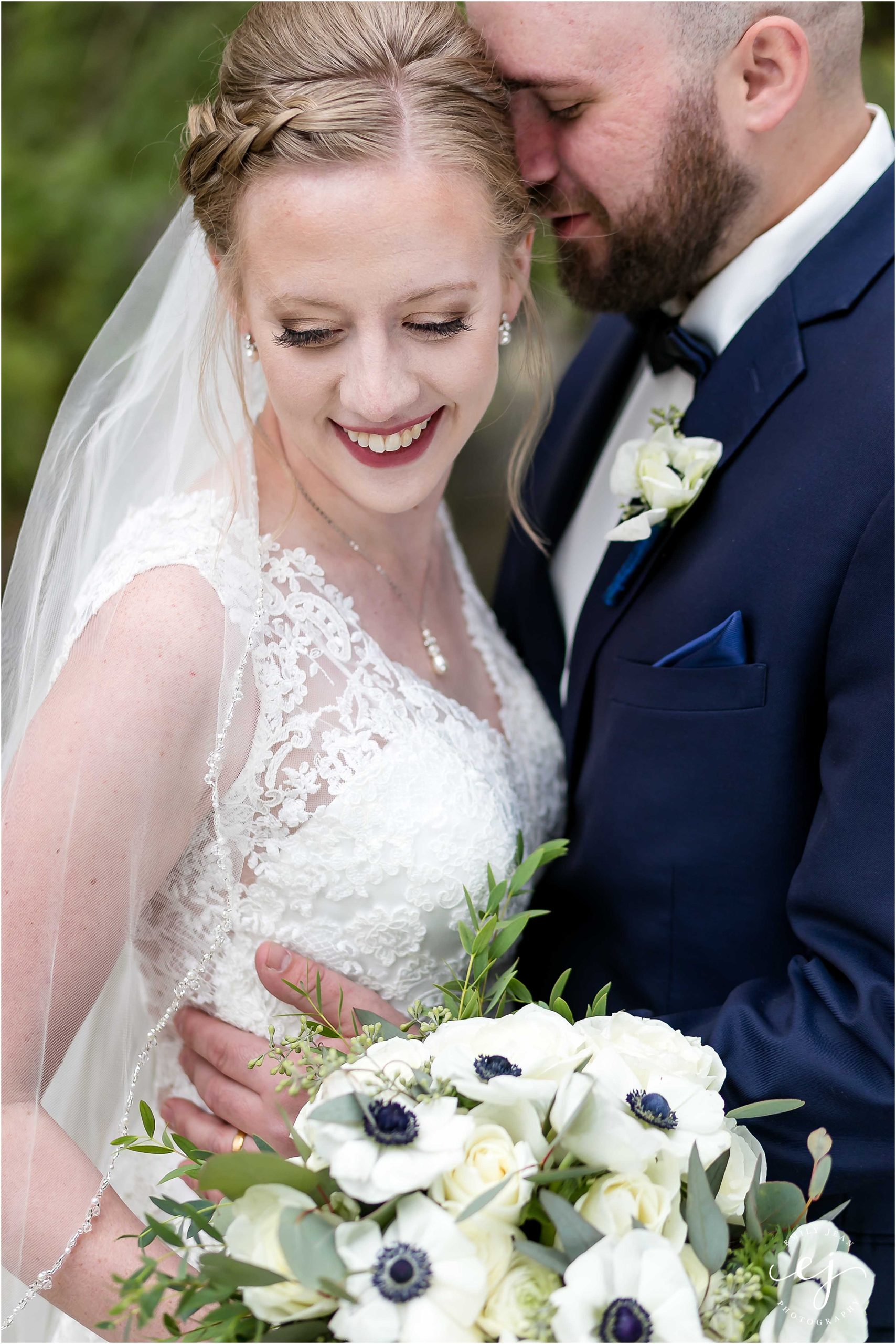 Bride and groom snuggling outside holding bouquet with dark navy center