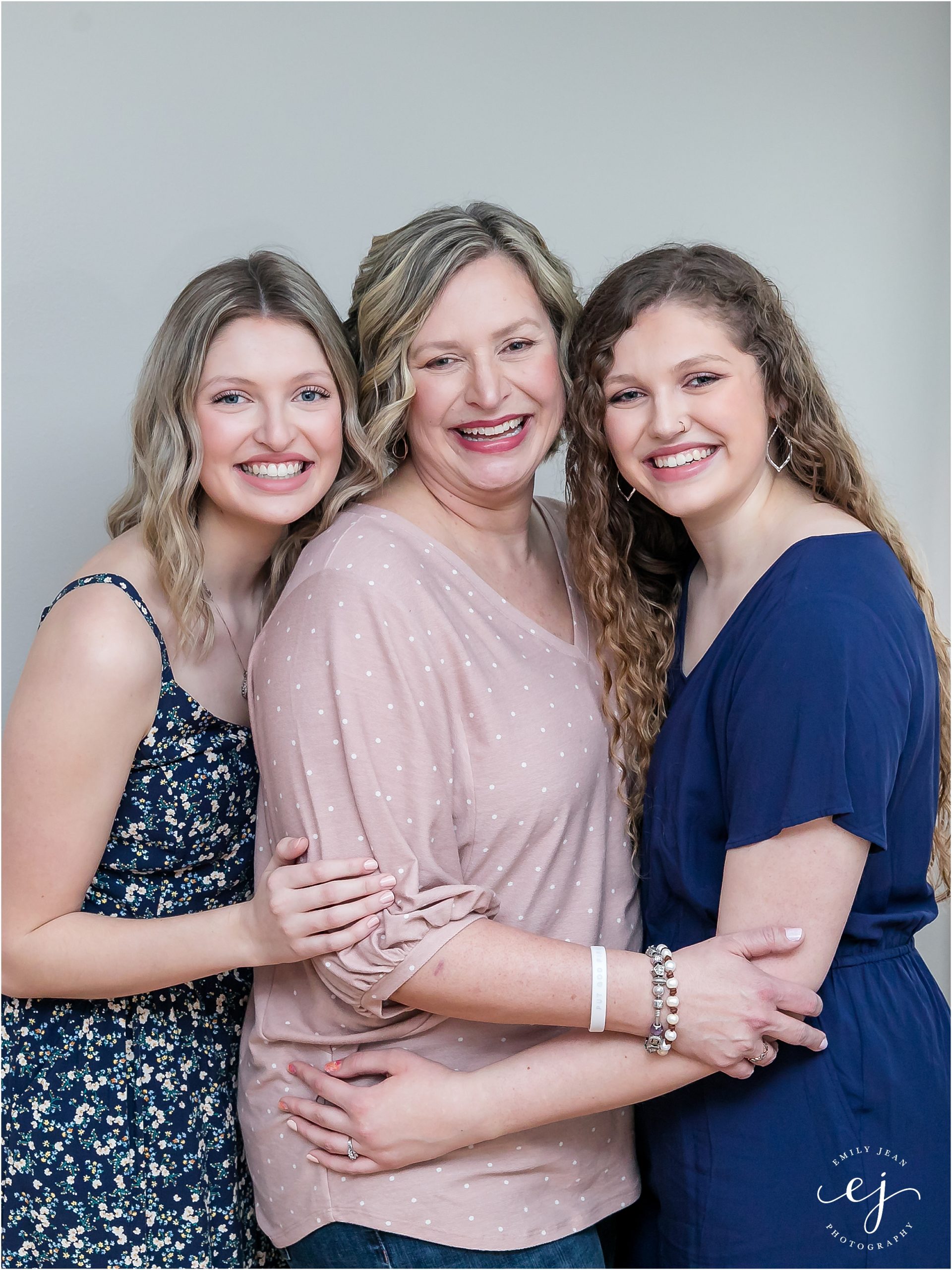 Mom and her adult daughters hugging smiling and looking at the camera