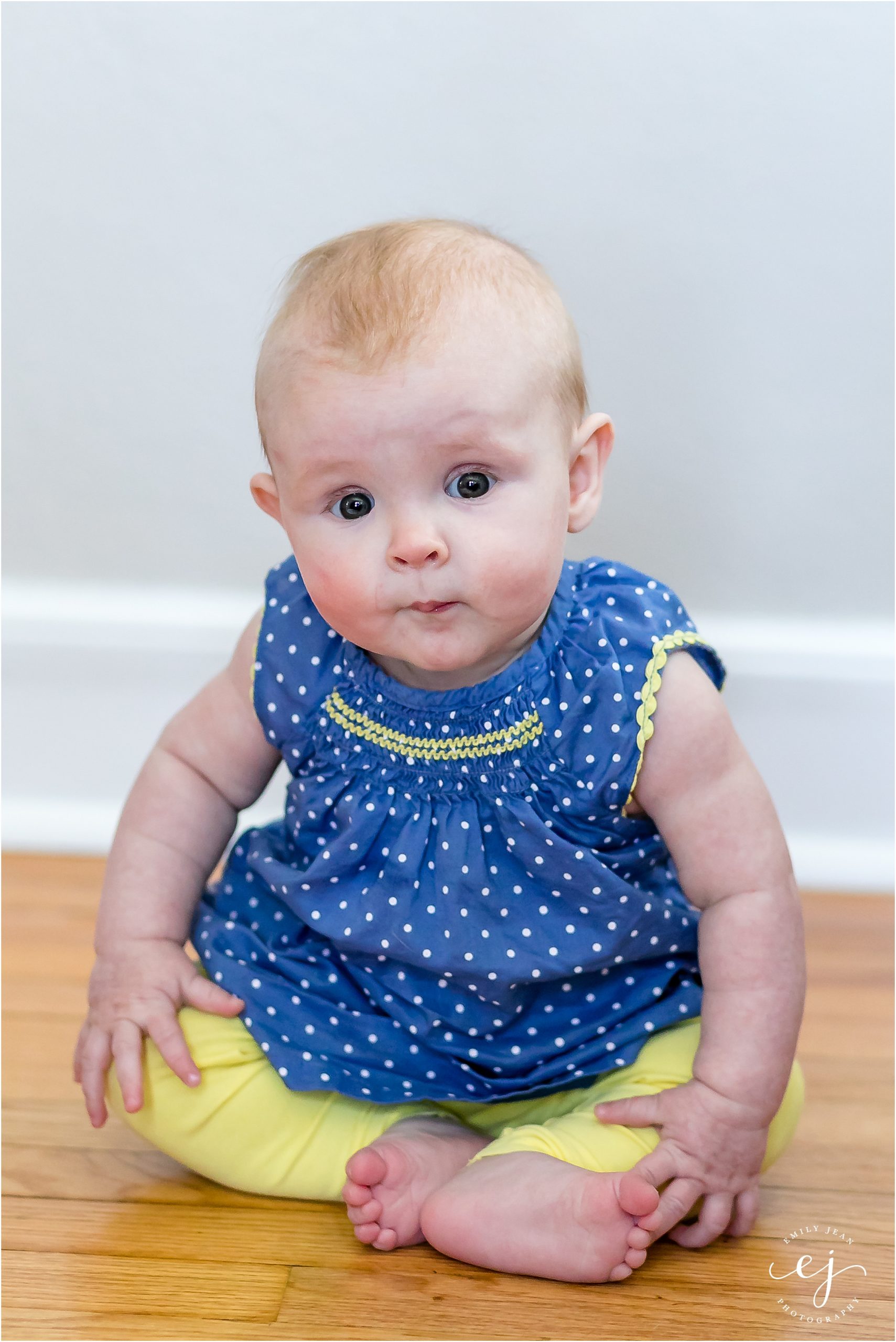 Five month old baby girl sitting on her own and blue shirt and yellow pants