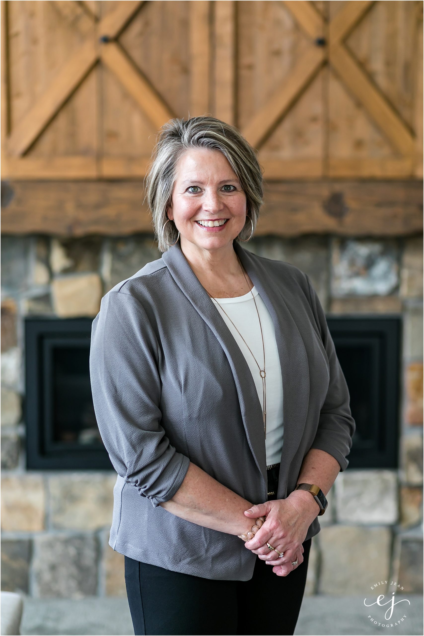 Real estate agent professional photo middle aged woman wearing gray blazer in front of fireplace