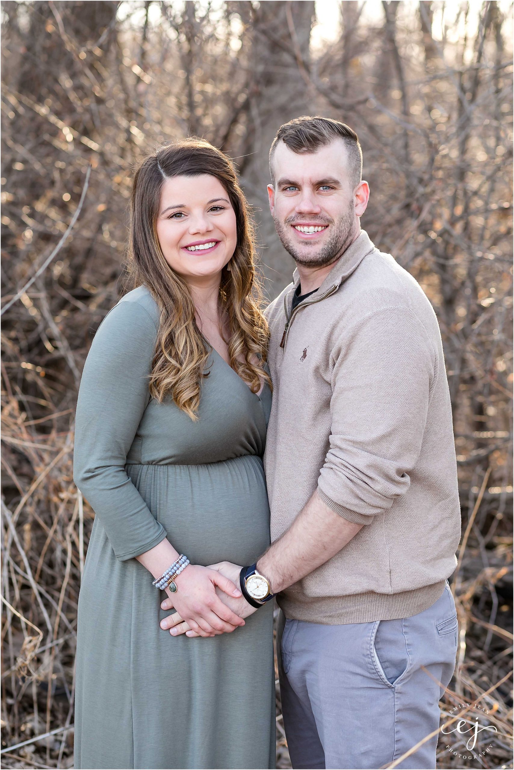 husband and wife smiling at the camera and hands on baby bump