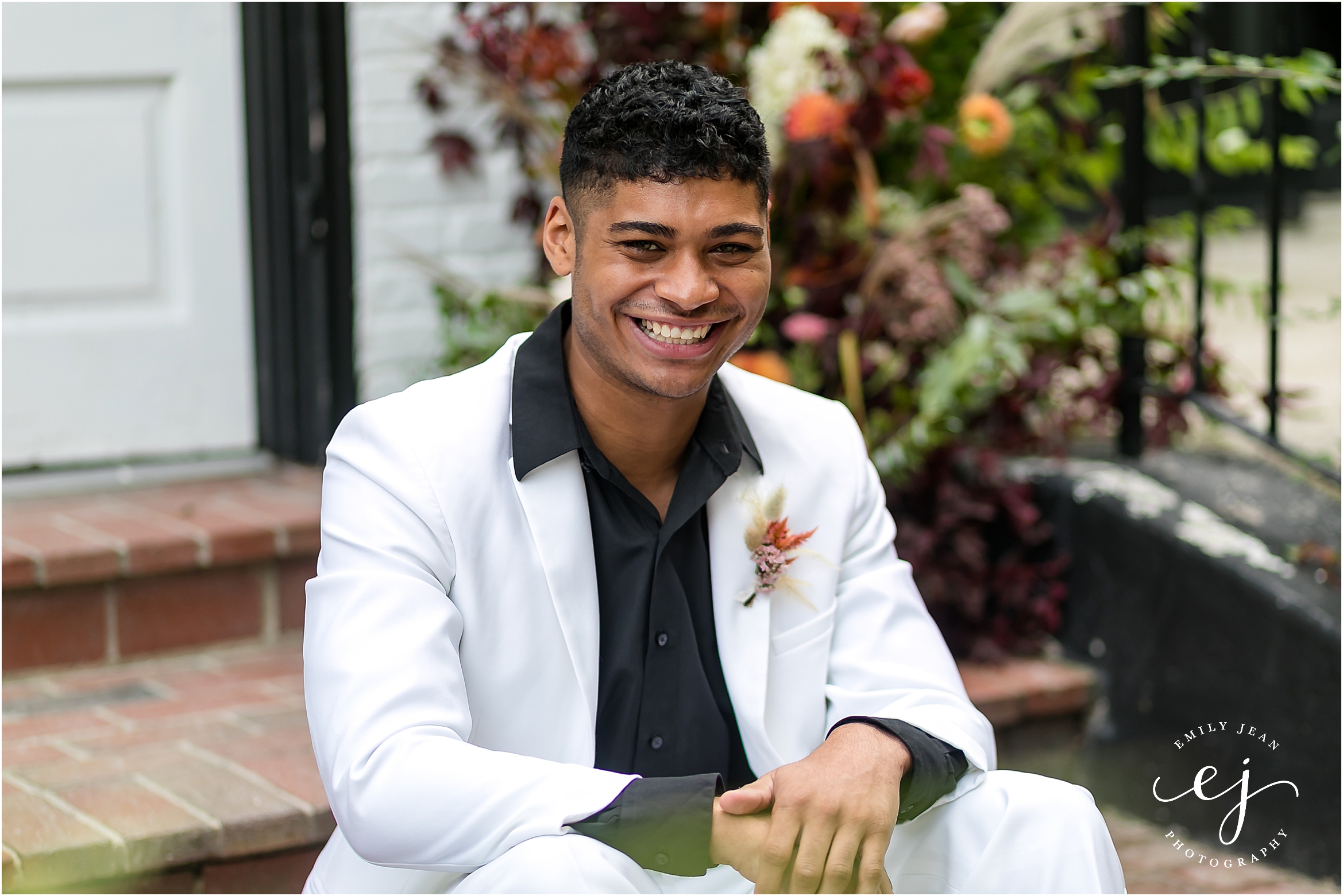 white suit and black shirt groom smiling leaning forward