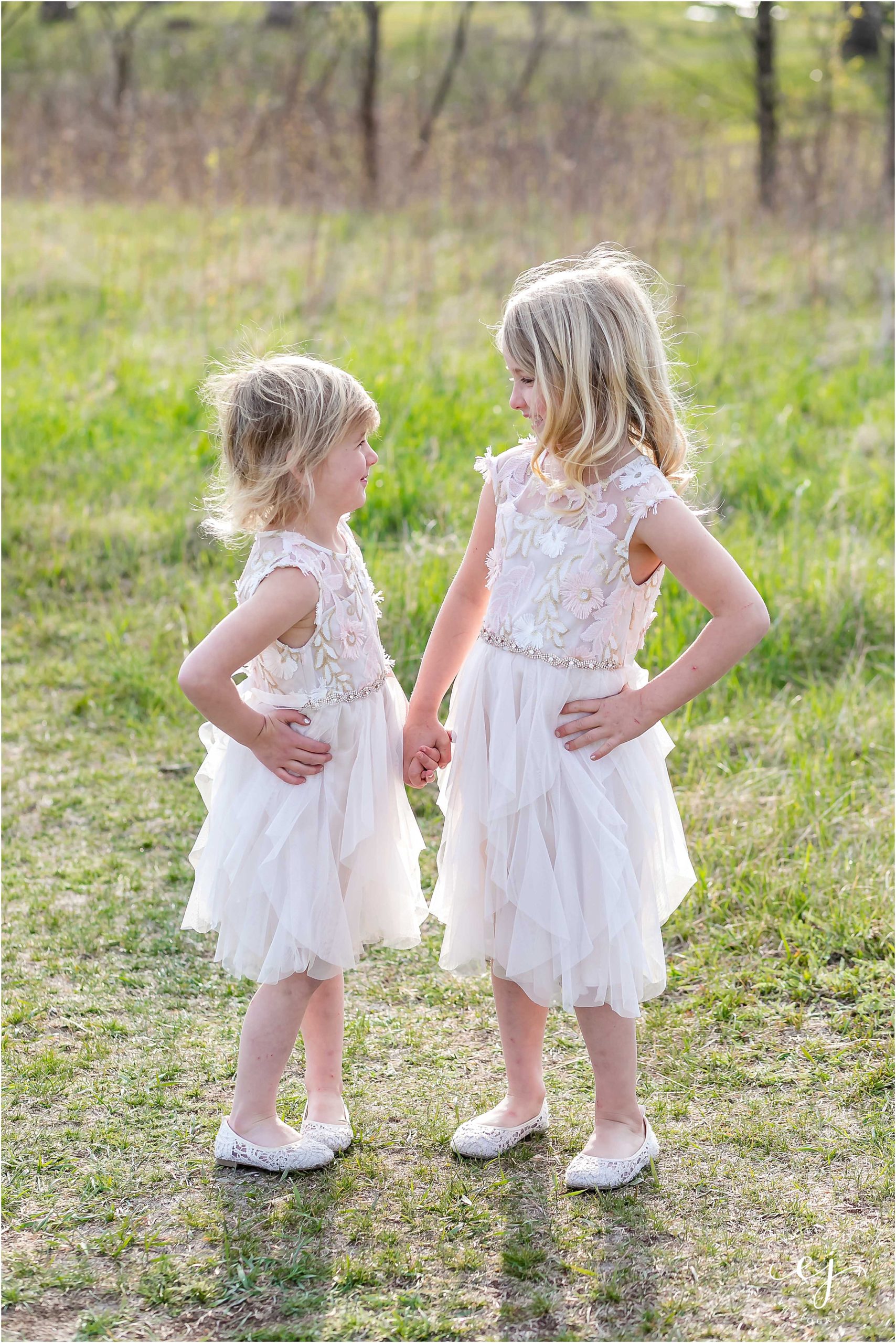 Two little blonde girls holding hands and looking at each other at family photos