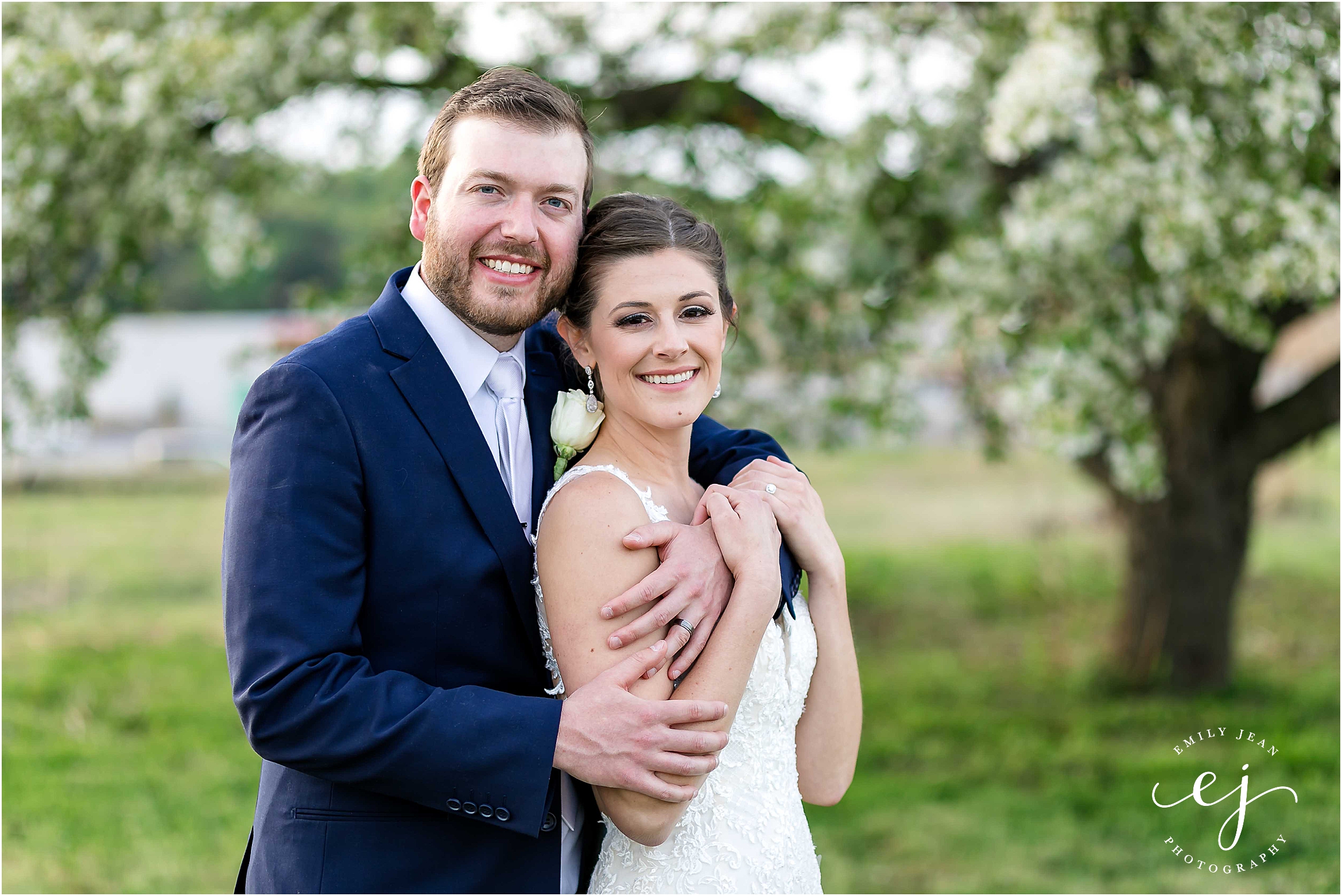 bride and groom standing in front of spring tree blooming with flowers