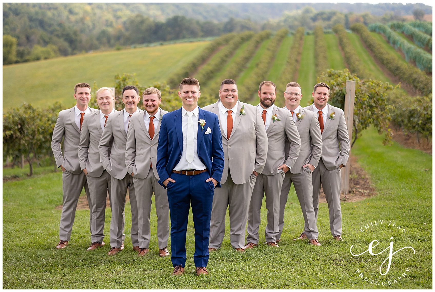 groom in navy and groomsmen in tan suits standing in the vineyard at pedretti party barn
