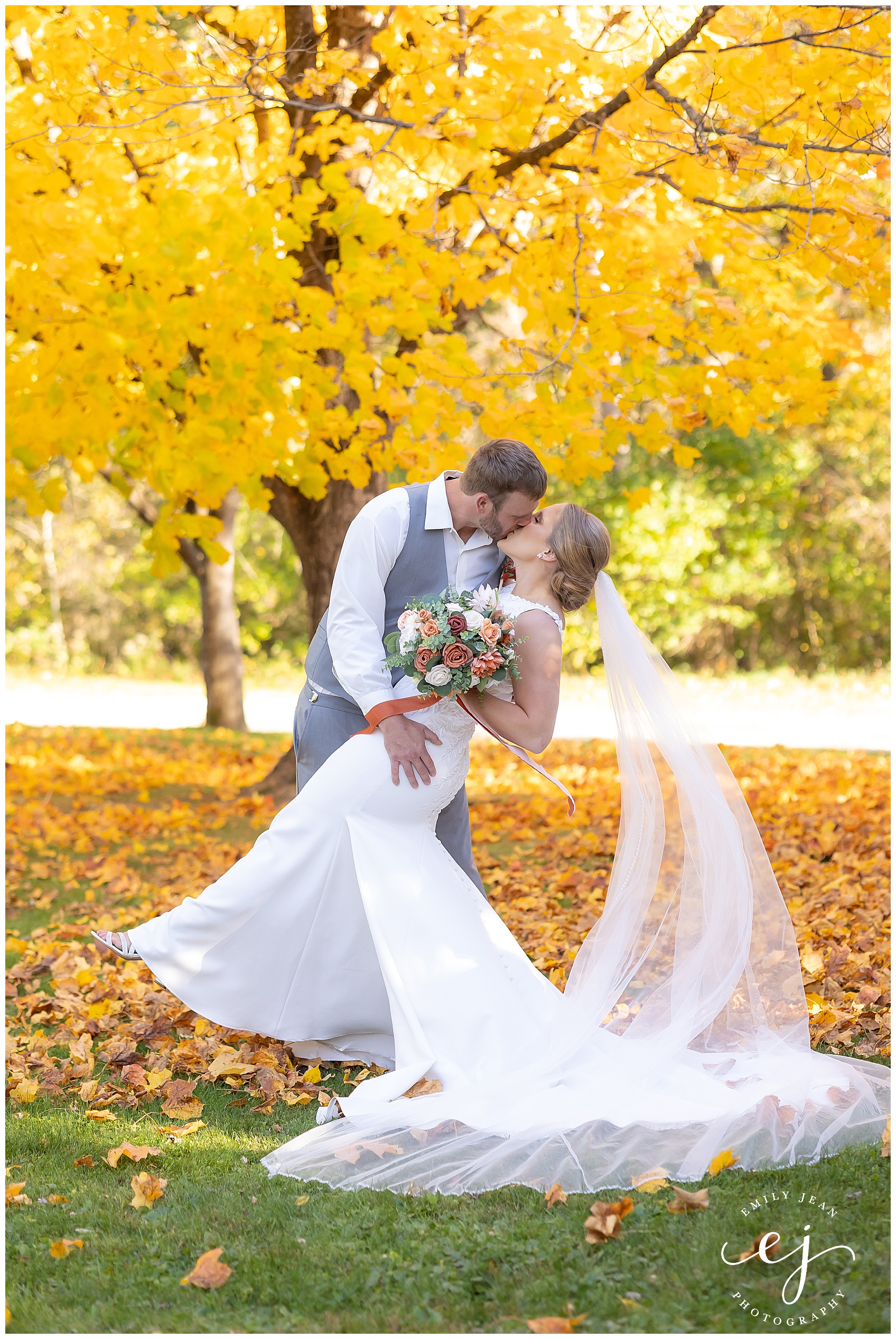 bride and groom dip and kiss in pile of leaves