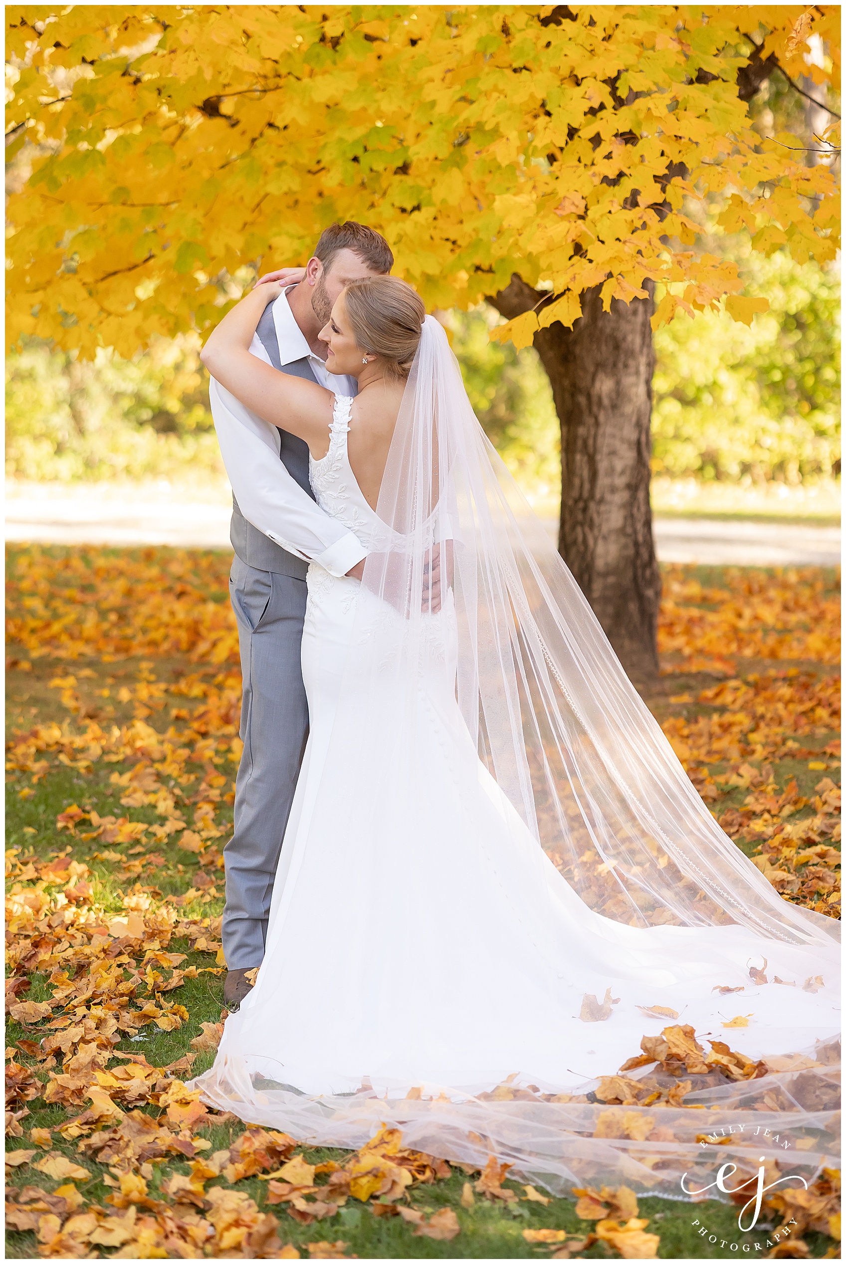 bride and groom standing near a yellow tree in autumn
