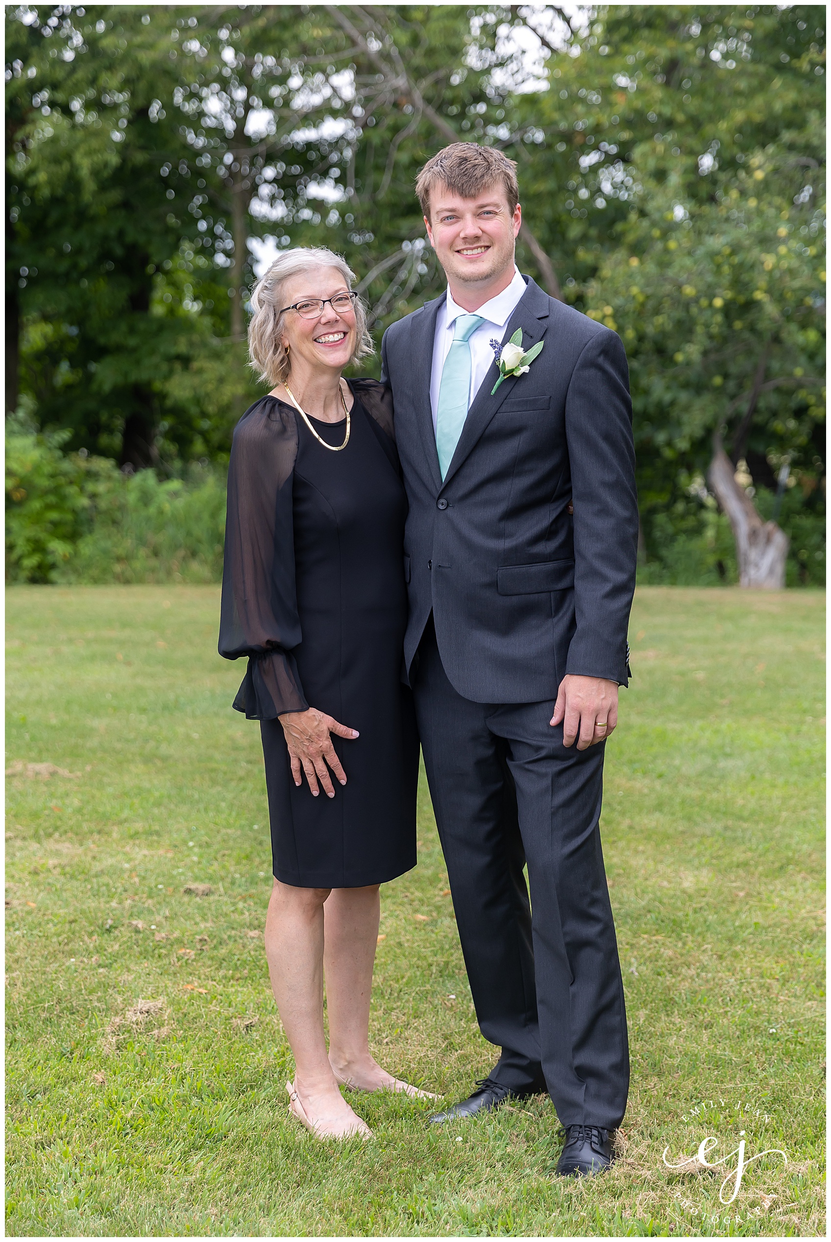 groom and his mom smiling at camera in grass field