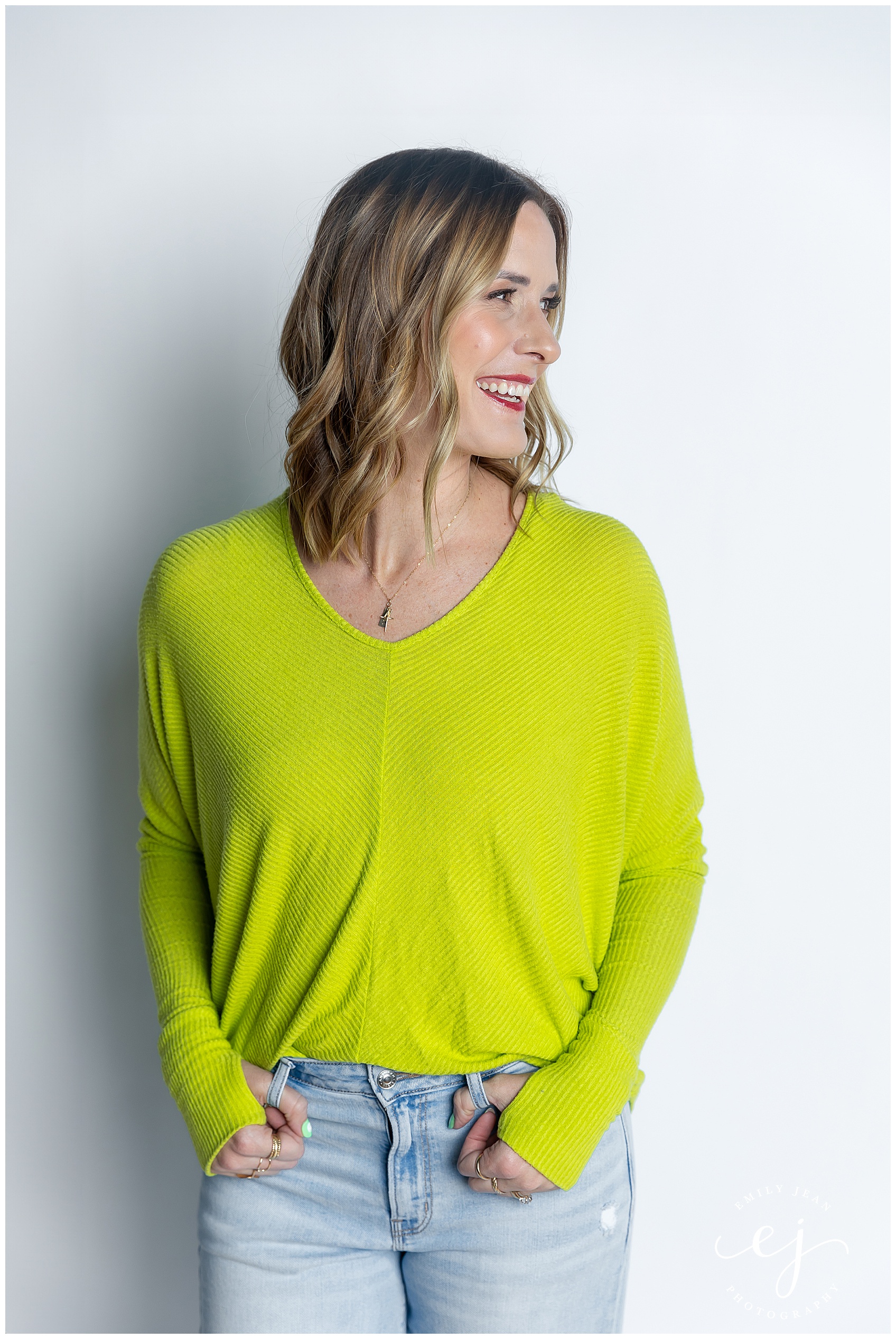 Anna Ledebuhr, coulee boutique models lime, green sweater with blue jeans against a white backdrop