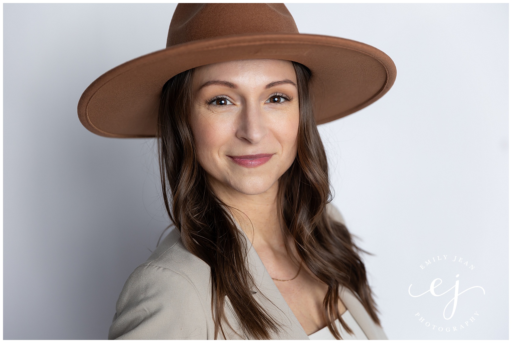 Leslie from Bella botanicals poses in front of a white backdrop with a flat brimmed hat. She is the owner of an organic skin care spa.